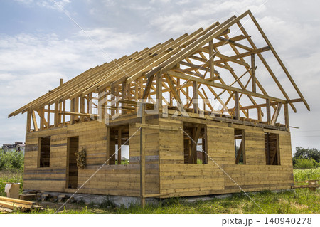 New cottage of natural ecological lumber materials under construction in green field. Wooden walls and steep roof frame. Property, investment, professional building and reconstruction concept. New cottage of natural ecological lumber materials under construction in green field. Wooden walls and steep roof frame. Property, investment, professional building and reconstruction concept. 140940278