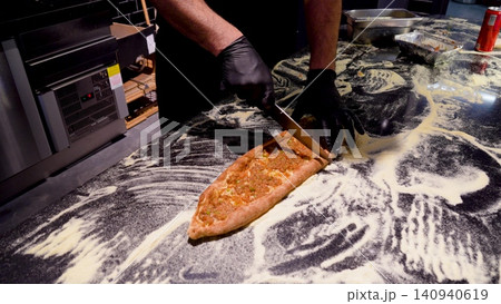 Man cutting Kasarli sucuklu pide and kiymali pide on the table in the bakery. Traditional Turkish flatbreads with meat and cheese toppings. Man cutting Kasarli sucuklu pide and kiymali pide on the table in the bakery. Traditional Turkish flatbreads with meat and cheese toppings. 140940619