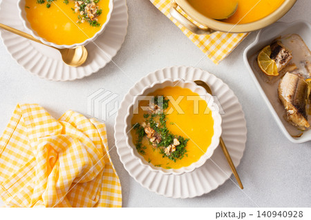 A meal is served on a table with pumpkin cream soup in a bowl and baked hake on a plate. Lemon slices and herbs are used as toppings in a relaxed dining setting A meal is served on a table with pumpkin cream soup in a bowl and baked hake on a plate. Lemon slices and herbs are used as toppings in a relaxed dining setting 140940928