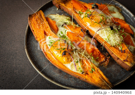 Nutrient-rich eggs baked inside sweet potatoes sit on a rustic plate. Fresh microgreens add a touch of bright color to this healthy meal served in a warm kitchen Nutrient-rich eggs baked inside sweet potatoes sit on a rustic plate. Fresh microgreens add a touch of bright color to this healthy meal served in a warm kitchen 140940968