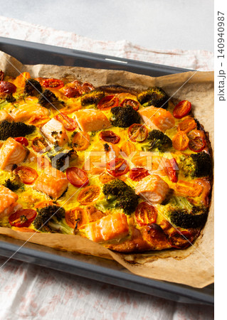 Salmon is baked along with broccoli, tomatoes, and eggs on a deck. This meal is set up for a healthy breakfast or lunch. The food looks fresh and ready to eat 140940987