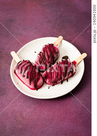 Three popsicles made from strawberries, bananas, beets, and Greek yogurt sit on a plate. They are drizzled with chocolate and enjoyed during a sunny day with friends Three popsicles made from strawberries, bananas, beets, and Greek yogurt sit on a plate. They are drizzled with chocolate and enjoyed during a sunny day with friends 140941000