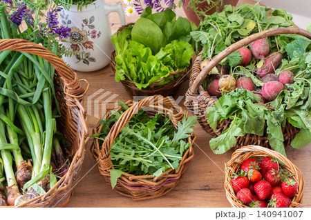 Baskets filled with fresh organic vegetables are placed on a wooden floor. Radishes, green onions, arugula, and lettuce create a colorful display of local produce 140941007