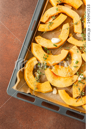 Butternut squash slices are arranged on a tray with herbs and garlic, ready for roasting. This is part of a cooking process in a kitchen setting Butternut squash slices are arranged on a tray with herbs and garlic, ready for roasting. This is part of a cooking process in a kitchen setting 140941018