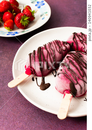 Three popsicles made from strawberries, bananas, beets, and Greek yogurt sit on a plate. They are drizzled with chocolate and enjoyed during a sunny day with friends Three popsicles made from strawberries, bananas, beets, and Greek yogurt sit on a plate. They are drizzled with chocolate and enjoyed during a sunny day with friends 140941032