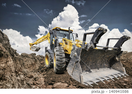 An excavator loader is working at a construction site. It is clearing dirt and rocks while clouds fill the sky. Heavy equipment is in use for a project An excavator loader is working at a construction site. It is clearing dirt and rocks while clouds fill the sky. Heavy equipment is in use for a project 140941086