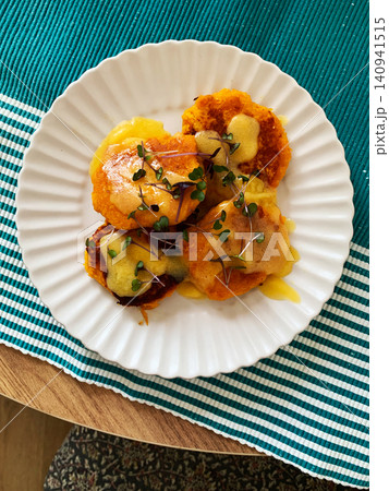 A plate of millet pancakes topped with hollandaise sauce and a poached egg sits on a table. This dish is offered as a healthy option for breakfast or lunch 140941515