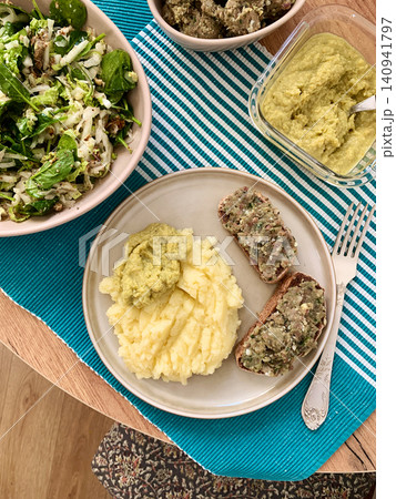 A plate shows a serving of boiled potatoes with hummus, a gluten free bread sandwich filled with herring mince, and fresh salad. This breakfast offers a nutritious start to the day 140941797