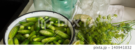 Cucumbers are being cleaned and sorted in a kitchen while glass jars are ready for canning. Ingredients are organized for preserving during the winter months ahead, banner Cucumbers are being cleaned and sorted in a kitchen while glass jars are ready for canning. Ingredients are organized for preserving during the winter months ahead, banner 140941832