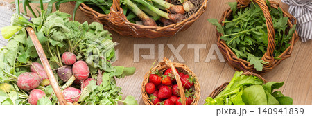 Baskets filled with fresh organic vegetables are placed on a wooden floor. Radishes, green onions, arugula, and lettuce create a colorful display of local produce, banner 140941839
