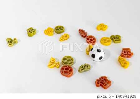 Soccer themed pasta shapes with a small soccer ball scattered on a white surface, creating playful football inspired food art. Soccer themed pasta shapes with a small soccer ball scattered on a white surface, creating playful football inspired food art. 140941929