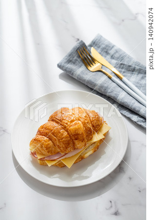 A golden croissant sandwich with ham and cheese on a white plate on a marble background A golden croissant sandwich with ham and cheese on a white plate on a marble background 140942074