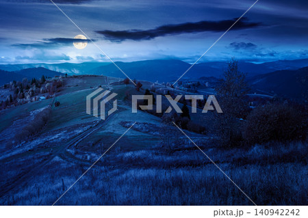 winding rural dirt path through hill at night. rolling countryside of ukraine in fall color. cloudy sky in full moon light. carpathian mountains in autumn winding rural dirt path through hill at night. rolling countryside of ukraine in fall color. cloudy sky in full moon light. carpathian mountains in autumn 140942242
