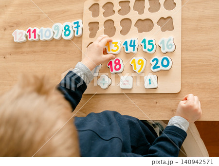 boy learns to count by laying out numbers from 1 to 20 on the board, boy 4-5 years old European appearance, at home in the living room sitting at the table, preparation for school. High quality photo boy learns to count by laying out numbers from 1 to 20 on the board, boy 4-5 years old European appearance, at home in the living room sitting at the table, preparation for school. High quality photo 140942571