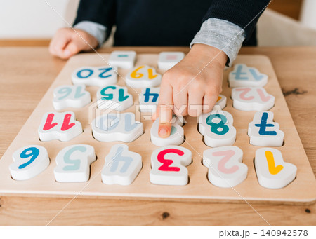 boy learns to count by laying out numbers from 1 to 20 on the board, boy 4-5 years old European appearance, at home in the living room sitting at the table, preparation for school. High quality photo boy learns to count by laying out numbers from 1 to 20 on the board, boy 4-5 years old European appearance, at home in the living room sitting at the table, preparation for school. High quality photo 140942578
