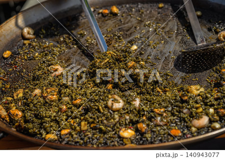 Close-up of black seafood paella with rice, shrimp and mussels cooked in large pan. Traditional Spanish arroz negro served at outdoor food event Close-up of black seafood paella with rice, shrimp and mussels cooked in large pan. Traditional Spanish arroz negro served at outdoor food event 140943077