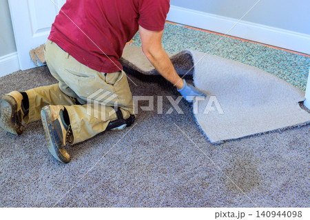 Handy worker is working on installing carpet in room removing old carpet preparing for new one. Handy worker is working on installing carpet in room removing old carpet preparing for new one. 140944098