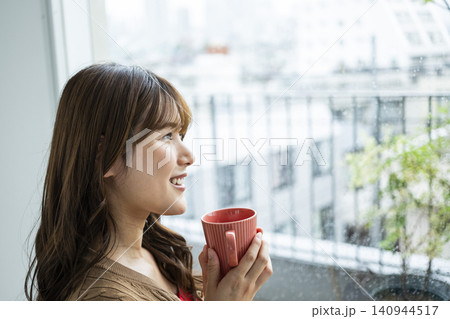 雨の日の窓際でコーヒーを飲む若い女性 140944517