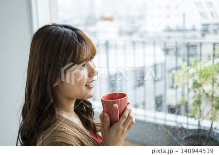 雨の日の窓際でコーヒーを飲む若い女性 140944519
