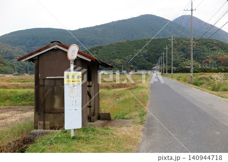 山間部の農地に伸びる直線の農道、道端に佇むバス停と、バス待ち用の小屋 山間部の農地に伸びる直線の農道、道端に佇むバス停と、バス待ち用の小屋 140944718