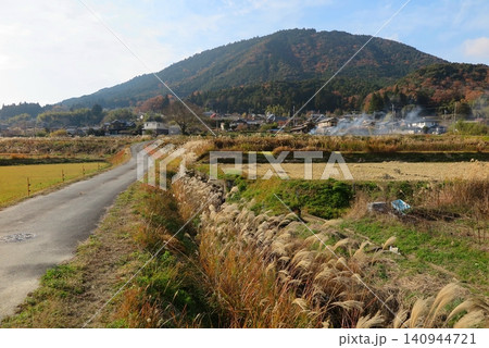 秋の里山、ゆるやかにカーブする農道と、道端のススキ、遠くに野焼きの煙 秋の里山、ゆるやかにカーブする農道と、道端のススキ、遠くに野焼きの煙 140944721