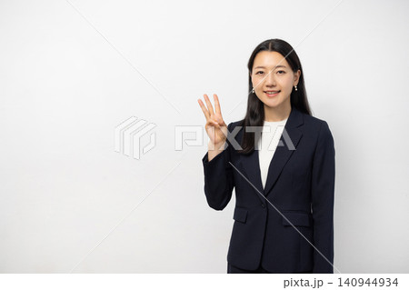 白い壁の前で指を3本立ててカメラ目線で微笑む若い日本人のビジネスウーマン 白い壁の前で指を3本立ててカメラ目線で微笑む若い日本人のビジネスウーマン 140944934