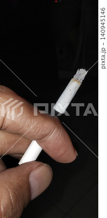 Hand holding lit cigarette with smoke on dark background Hand holding lit cigarette with smoke on dark background 140945146