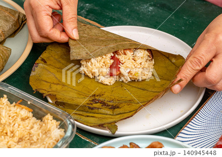 hands wrapping seasoned glutinous rice with chicken and Chinese sausage into a fresh lotus leaf. 140945448