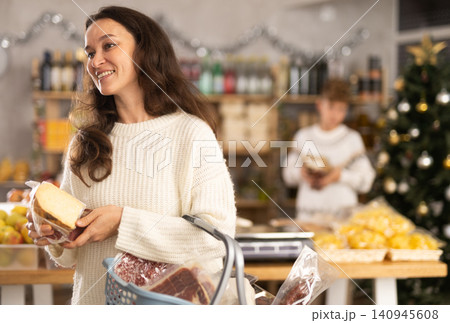 Portrait of female shopper with cart cheese and meat choosing food and wine for Christmas celebration in grocery department of shop 140945608