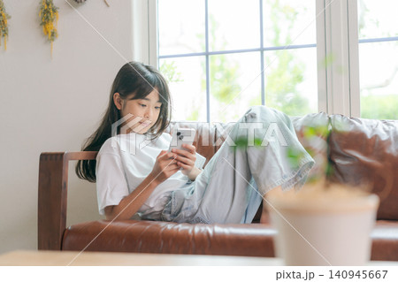 ソファでスマホを見る小学生 140945667