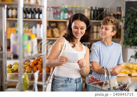 In store near snack display case, mom and son stand with paper list, recall planned products 140945715
