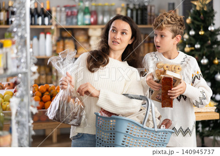 Adolescence boy with mother choose consider snacks in shop on eve of New Year Adolescence boy with mother choose consider snacks in shop on eve of New Year 140945737