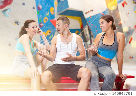 Young man and two women talking merrily sitting in climbing hangar Young man and two women talking merrily sitting in climbing hangar 140945791
