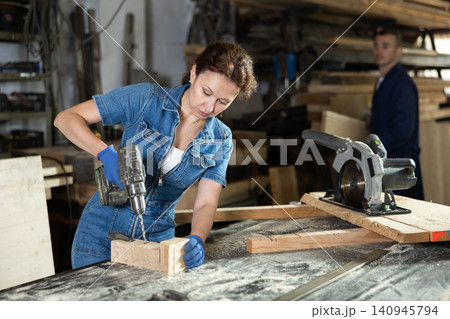 Adult woman drills hole in oak plank Adult woman drills hole in oak plank 140945794