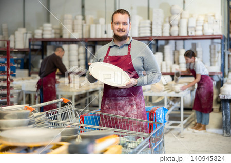 Enthusiastic ceramicist demonstrating handcrafted plates in ceramic studio Enthusiastic ceramicist demonstrating handcrafted plates in ceramic studio 140945824