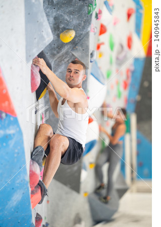 Young man climbing on artificial rock wall in rock-climbing gym Young man climbing on artificial rock wall in rock-climbing gym 140945843