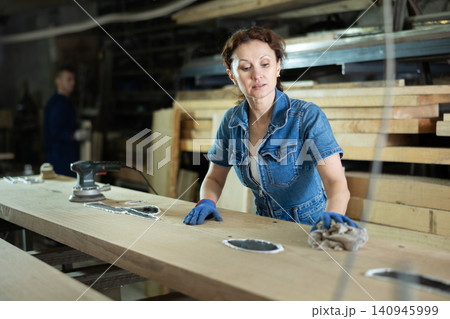 During manufacturing, woman employee grinds surface of wooden board, gives smoothness to surface During manufacturing, woman employee grinds surface of wooden board, gives smoothness to surface 140945999