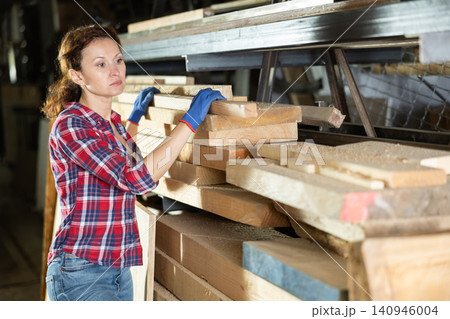 Woman employee of carpentry workshop takes out necessary board from stack of materials Woman employee of carpentry workshop takes out necessary board from stack of materials 140946004