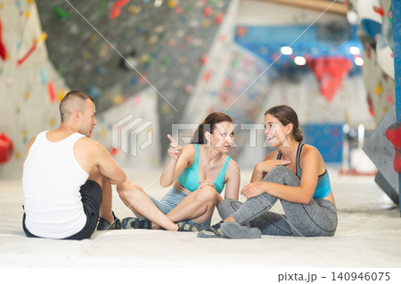 Young man and two women talking merrily sitting on floor in climbing hangar Young man and two women talking merrily sitting on floor in climbing hangar 140946075