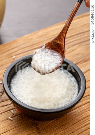 close-up of a wooden spoon scooping fermented sweet rice wine above a black bowl on a wooden board. close-up of a wooden spoon scooping fermented sweet rice wine above a black bowl on a wooden board. 140946116
