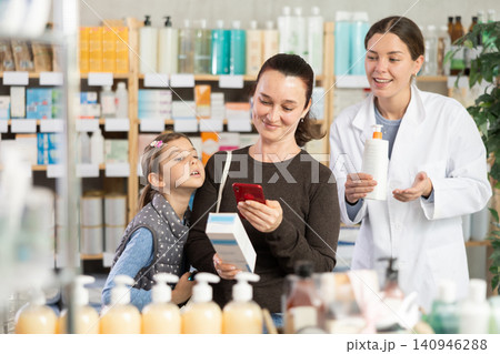 Woman with preteen daughter scanning QR code on body cream in pharmacy 140946288