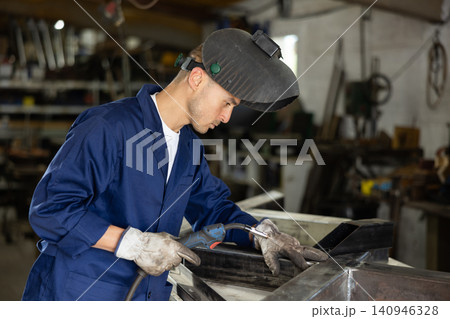 Young man welding metal part in workshop Young man welding metal part in workshop 140946328