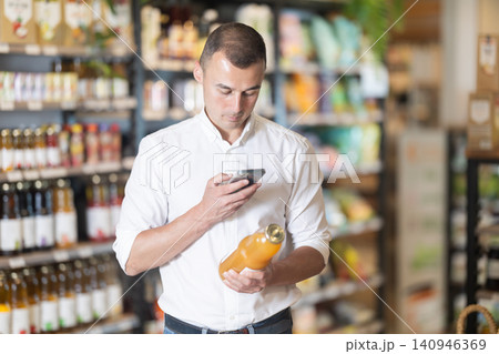 Man scanning barcode on juice bottle with smartphone in store 140946369