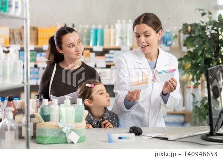 Pharmacist recommending medicines to mom with child at drugstore counter Pharmacist recommending medicines to mom with child at drugstore counter 140946653