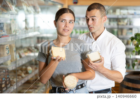 Positive young couple choosing cheese in large supermarket Positive young couple choosing cheese in large supermarket 140946660