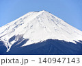 青空の下でベッタリ冠雪して白く化粧した富士山頂と森林限界以下の木々に着雪して鼠色になった樹林の裾野 140947143