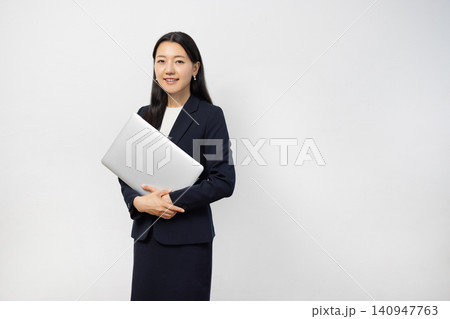 白い壁の前でノートパソコンを持ってカメラ目線で微笑む若い日本人のビジネスウーマン 白い壁の前でノートパソコンを持ってカメラ目線で微笑む若い日本人のビジネスウーマン 140947763