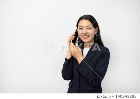 白い壁の前でスマートフォンを耳に当てて話す若い日本人のビジネスウーマン 140948195