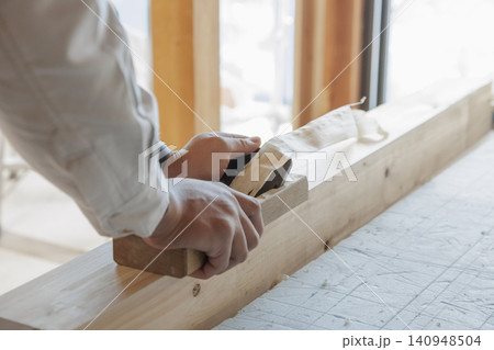 窓辺の光の中で角材に鉋をかける職人の手元木材の表面仕上げ作業 窓辺の光の中で角材に鉋をかける職人の手元木材の表面仕上げ作業 140948504