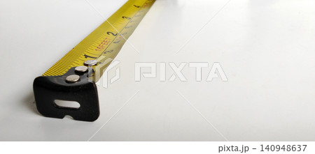 Close-up photo of a yellow tape measure with metric and imperial scales on a white background. 140948637
